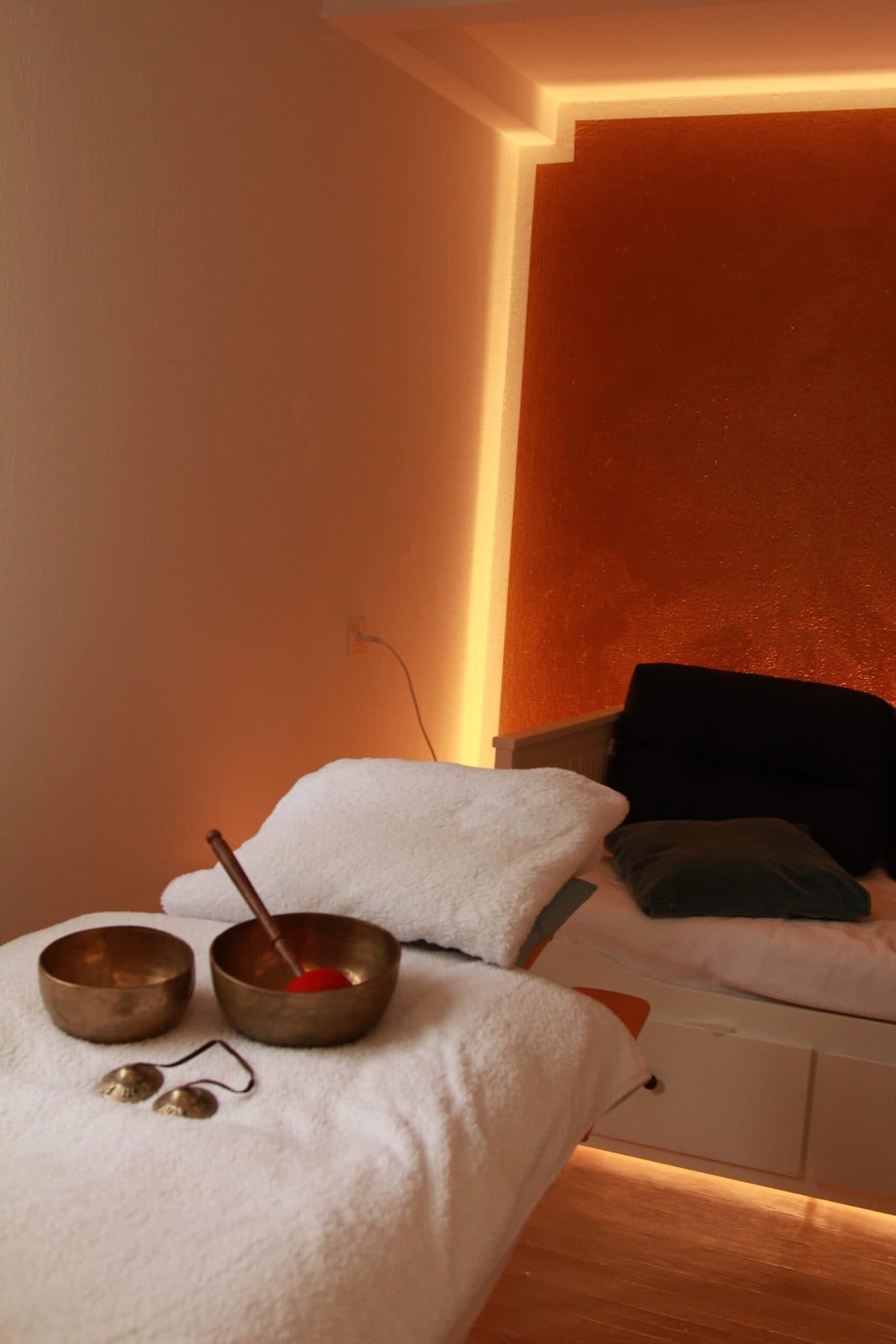 Massageliege mit Klangschalen vor warm beleuchteter Akzentwand