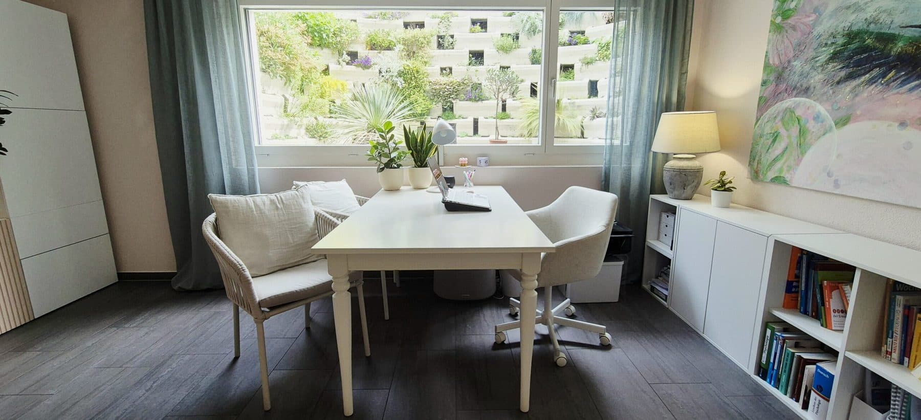 Helles Arbeitszimmer mit weissem Tisch und Blick auf eine begrünte Fassade