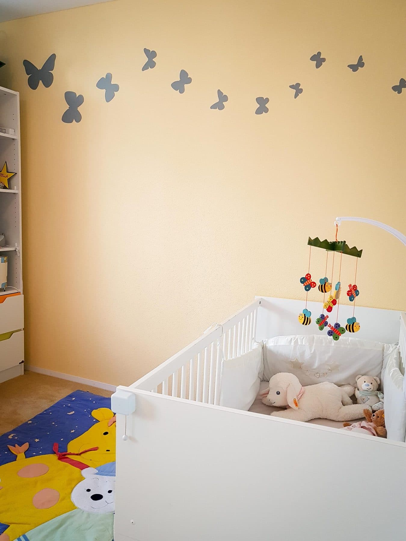 Babyschlafzimmer mit gelber Wand, Schmetterlingen und weissem Gitterbett