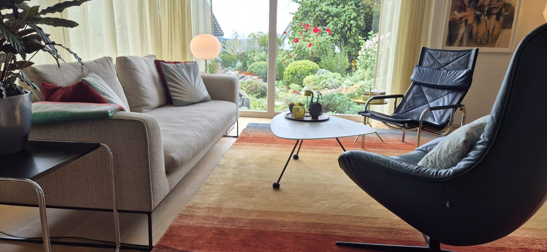 Helles Wohnzimmer mit beigem Sofa, Ledersesseln und Blick in den Garten
